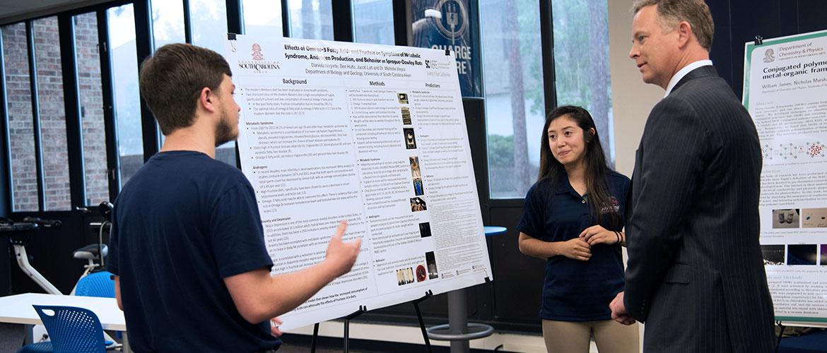 Students presenting information (on a poster board) to the Provost